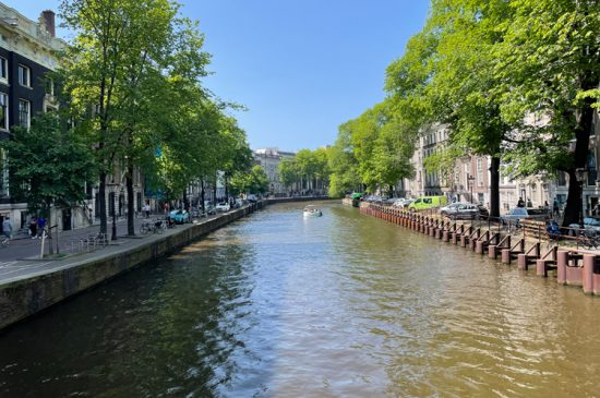 Boot op een Amsterdamse gracht tussen bomen en historische grachtenpanden